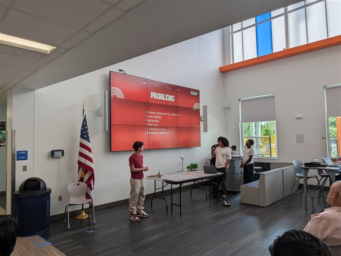 A student team pitches a restaurant-efficiency AI concept to the group.